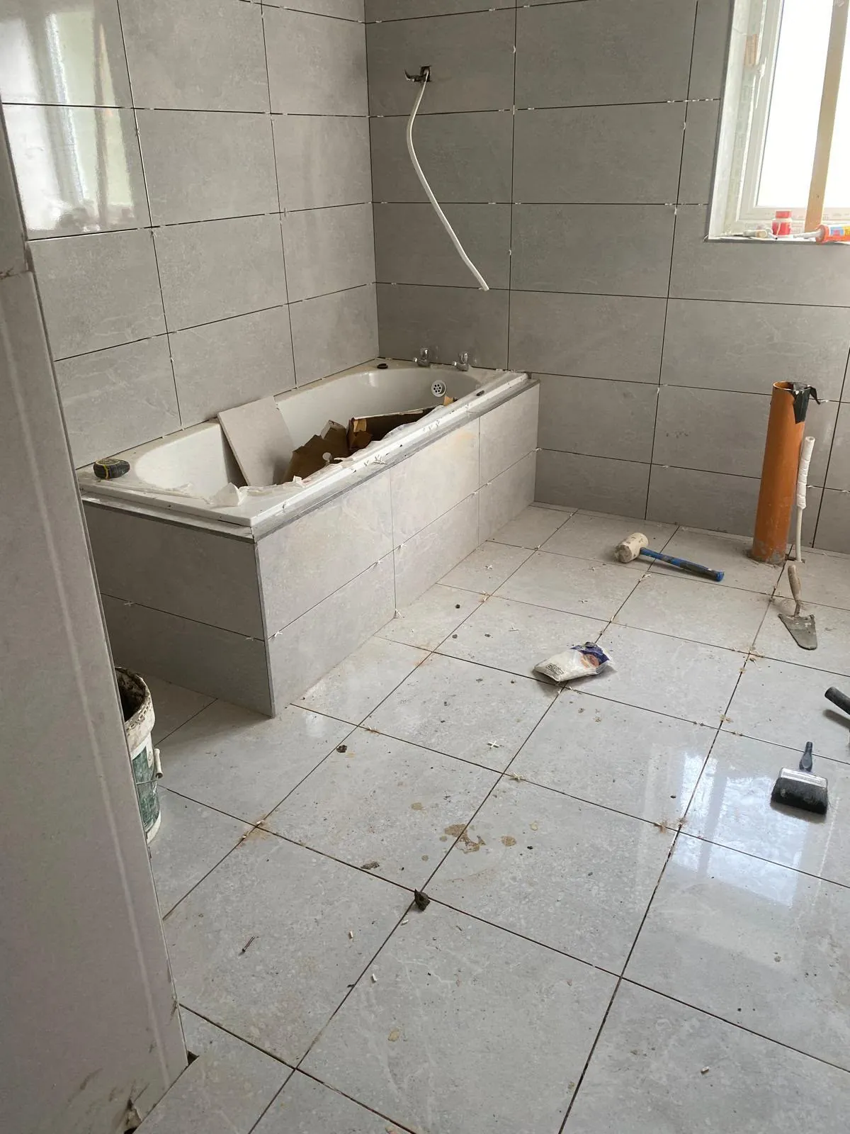 Bathroom mid-renovation with tiling under way and the old bath being removed